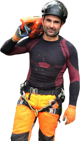 Jonathan, casque et tenue de grimpe, tronçonneuse à l'épaule, regard caméra